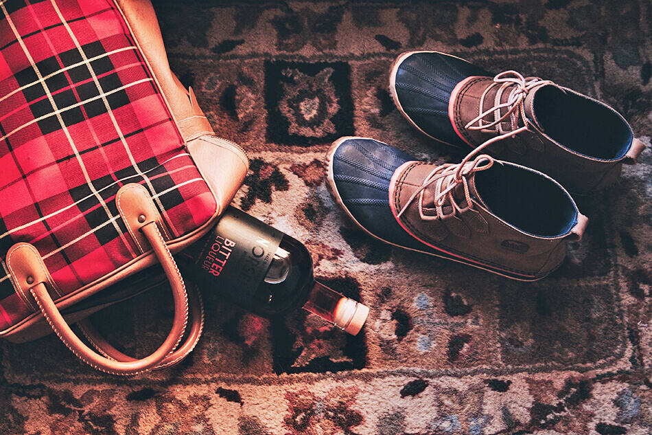 Tartan bag, a bottle of wine and winter hiking boots on a rug