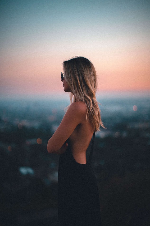Girl wearing a black evening dress with naked back watches Waikiki at sunset