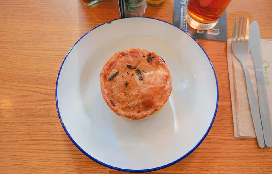 A golden-brown British meat pie on a white plate