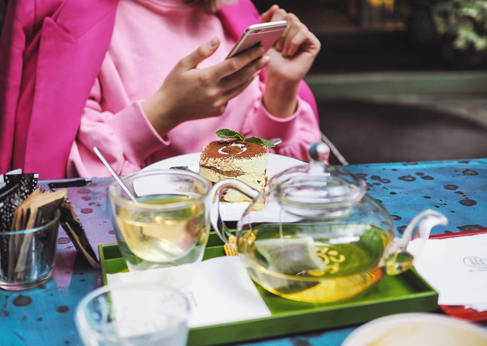 Woman dressed in pink texts while drinking tea in London