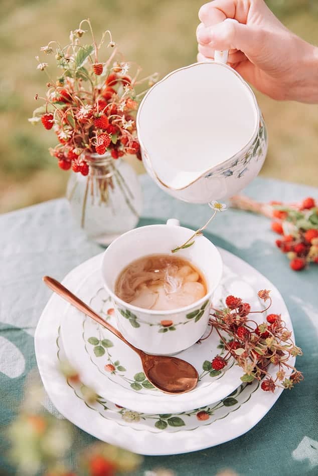 Woman serving herself a strawberry tea in a China cup