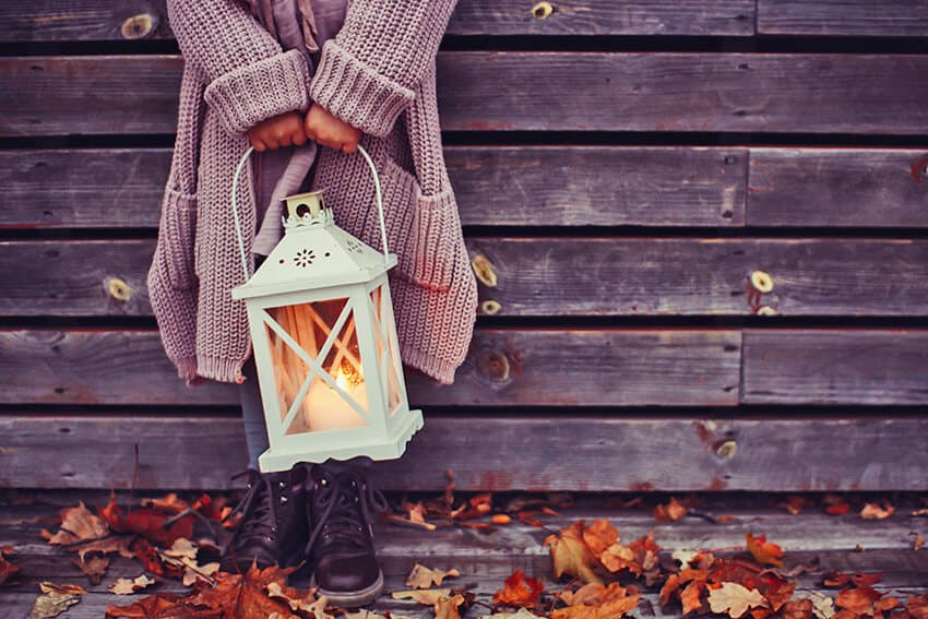A little girl holding a lantern against a cabin in the Adirondacks in autumn