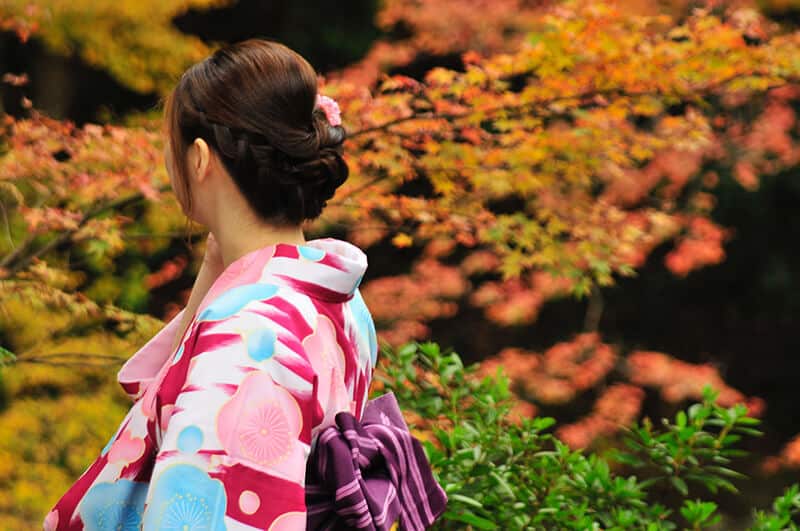 Fall trip to Japan: beautiful maiko wearing a kimono in a park in autumn