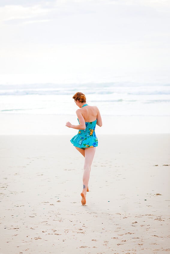 Una donna saltella in spiaggia con indosso un costume intero stile vintage