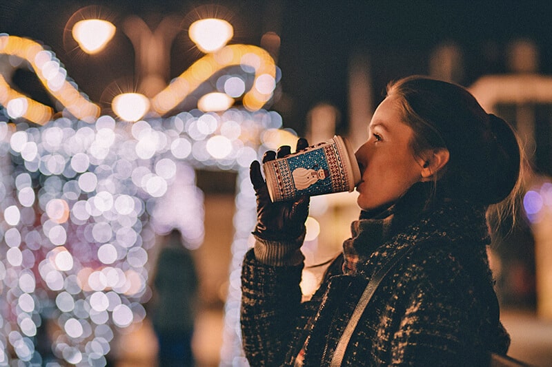 Ragazza beve da un bicchiere festivo mentre esplora i migliori mercatini di Natale in Italia