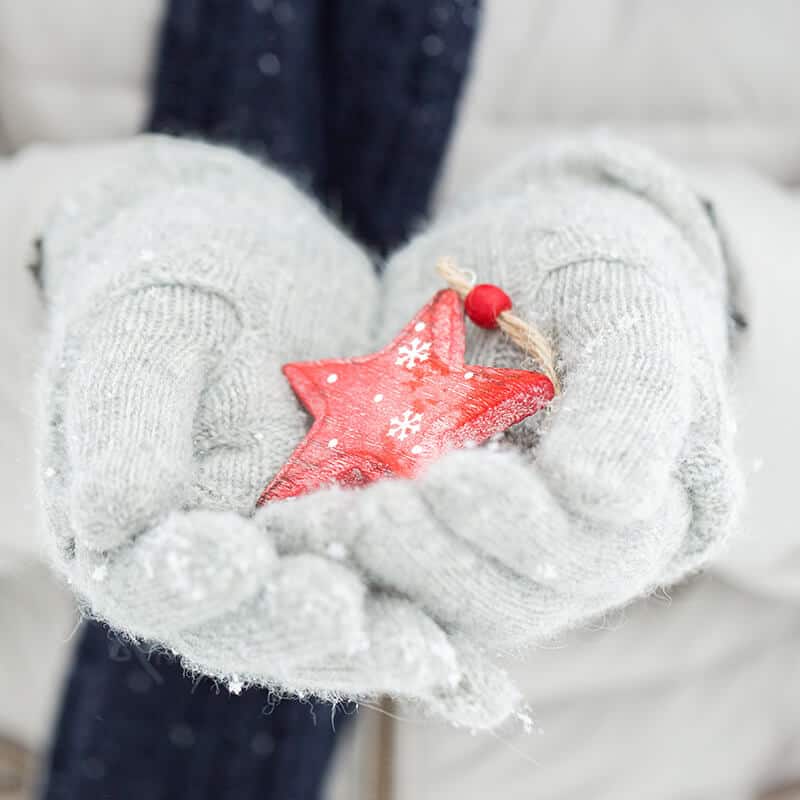 Girl holding a wooden Christmas ornament with gloved hands