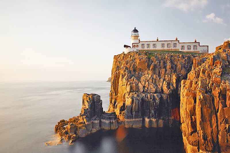 A lighthouse on a steep cliff at sunset in Scotland