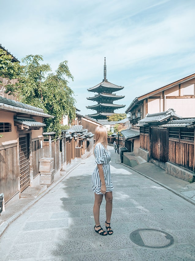 Blonde girl enjoying a day trip to Kyoto with a tall pagoda at her back