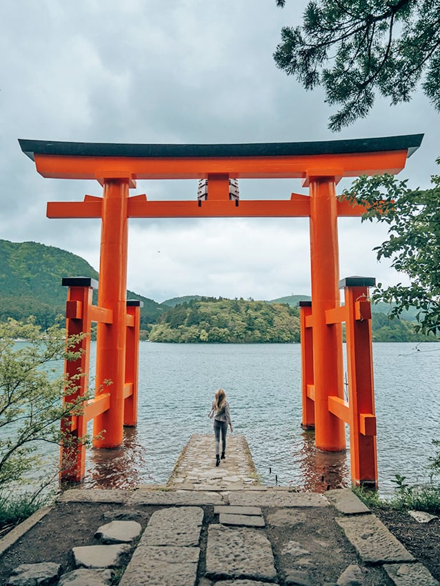 Woman walking through a torii gate on a lake at Hakone Shrine in Japan