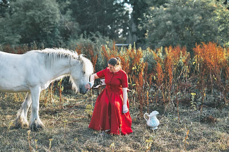 Donna in abito rosso con un cavallo bianco esplora i paesaggi irlandesi