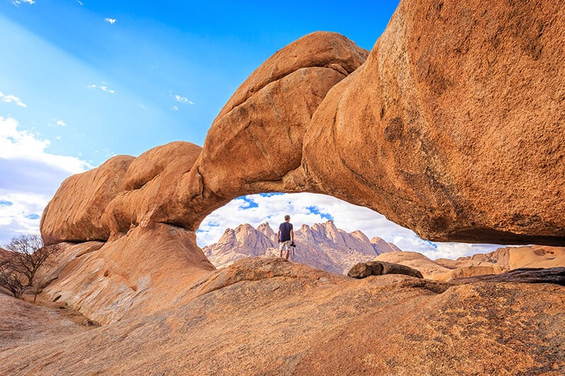 Fotografo passeggia sotto un massiccio arco in pietra ad Arches (Utah)