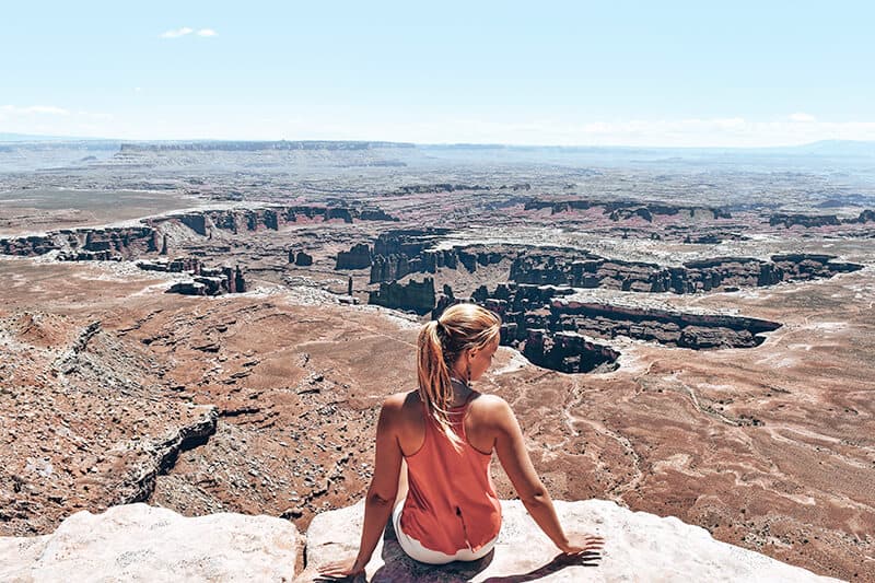 Hiker sitting on a rock while looking at Island in the Sky at Canyonlands (Utah)