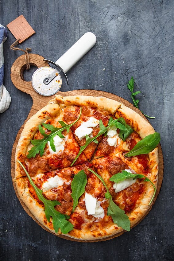 Neapolitan pizza margherita on a dark grey table with arugula on the top