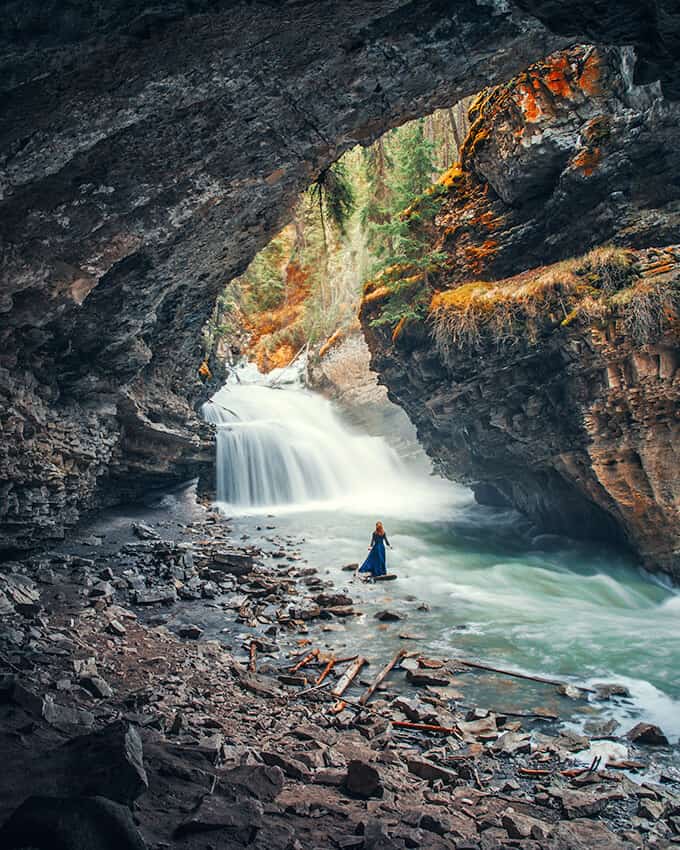 Woman in a long blue dress in a river with a small waterfall in the background