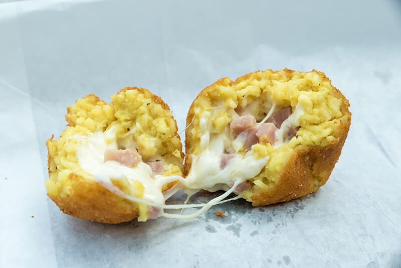 Neapolitan arancino cut in half to show mozzarella an bits of Italian baked ham