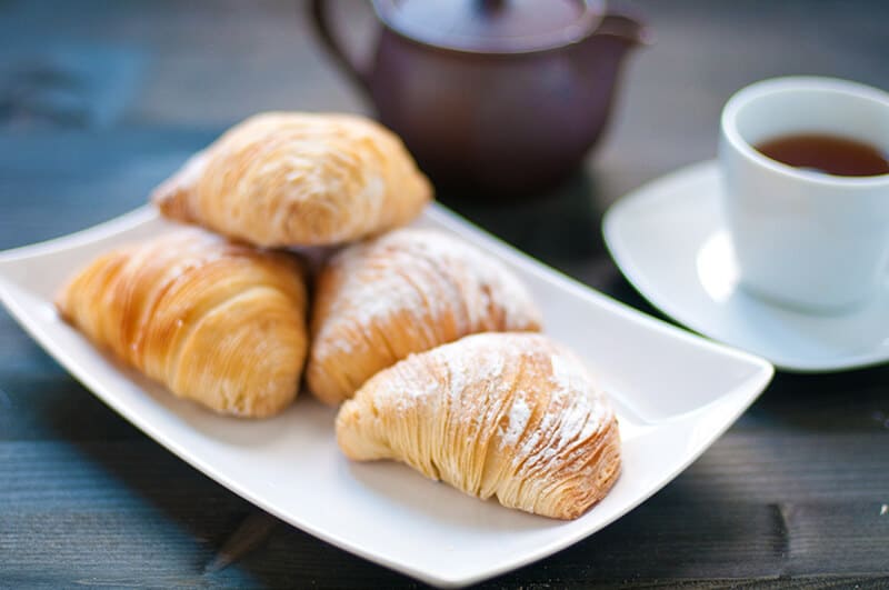 Four sfogliatella riccia on a plate served with a cup of Neapolitan espresso