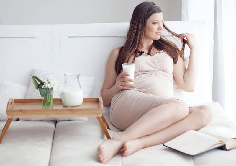 Pregnant woman laying on the bed while looking out of the window