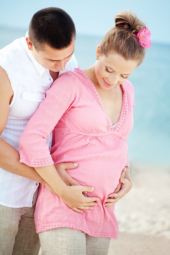 Pregnant couple celebrating a babymoon on a budget on the beach