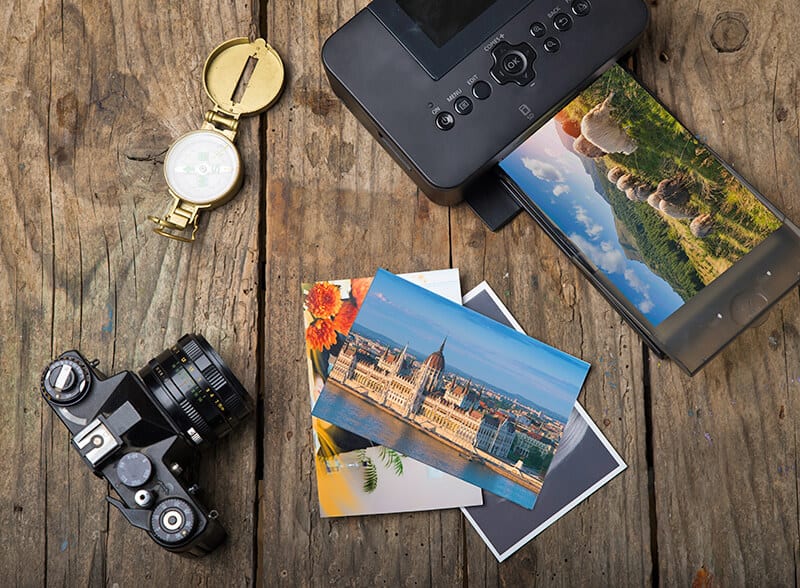 Fotocamera digitale e stampante accanto a un mucchio di foto di viaggio