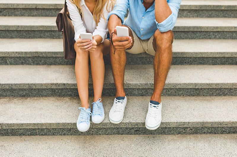 Couple sitting on a marble staircase in Italy while holding their cellphones