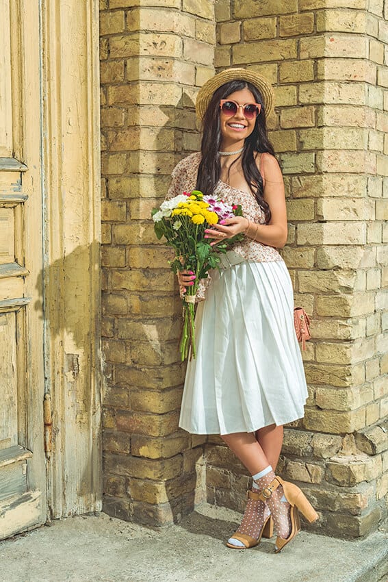 Young woman wearing a white dress, sunglasses, hat and sporting fresh flowers on her Italian honeymoon