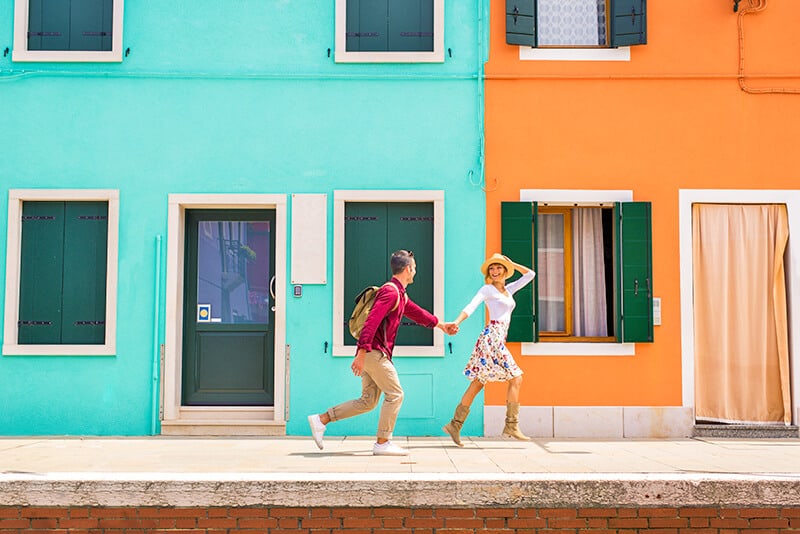 Couple on honeymoon running in Burano (Italy) next to the colorful houses