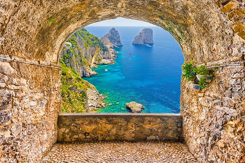 Panorama romantico dei Faraglioni di Capri visti attraverso un arco in pietra