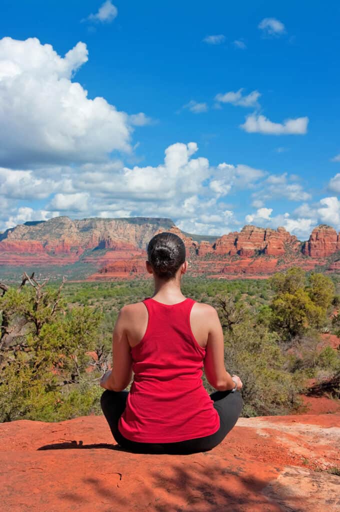 Woman wearing a red tank top is meditating on a vortex near Sedona in Arizona