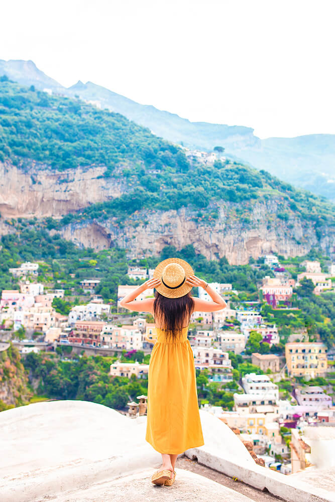 Woman wearing a yellow sundress is overlooking Positano on the Amalfi Coast 