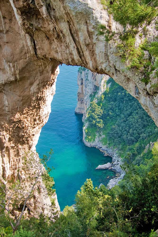 Massiccio arco roccioso attraverso il quale si vede la costa di Capri e il mare blu