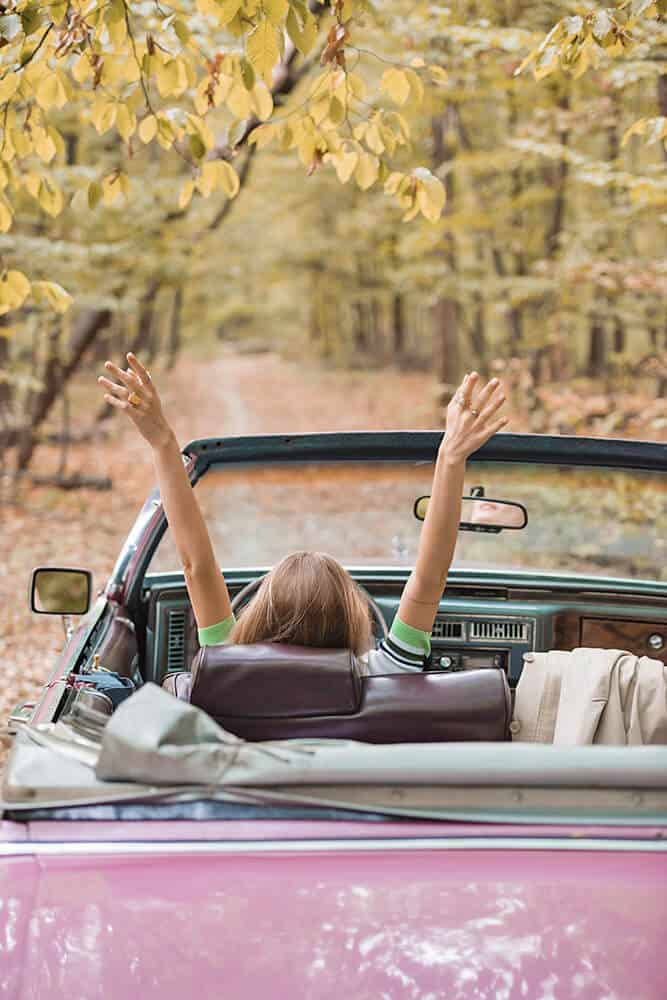 Ragazza alla guida di una cadillac rosa nella foresta