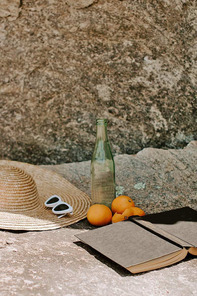 Straw hat, sunglasses, oranges and a book on a boulder beach in Naples Italy