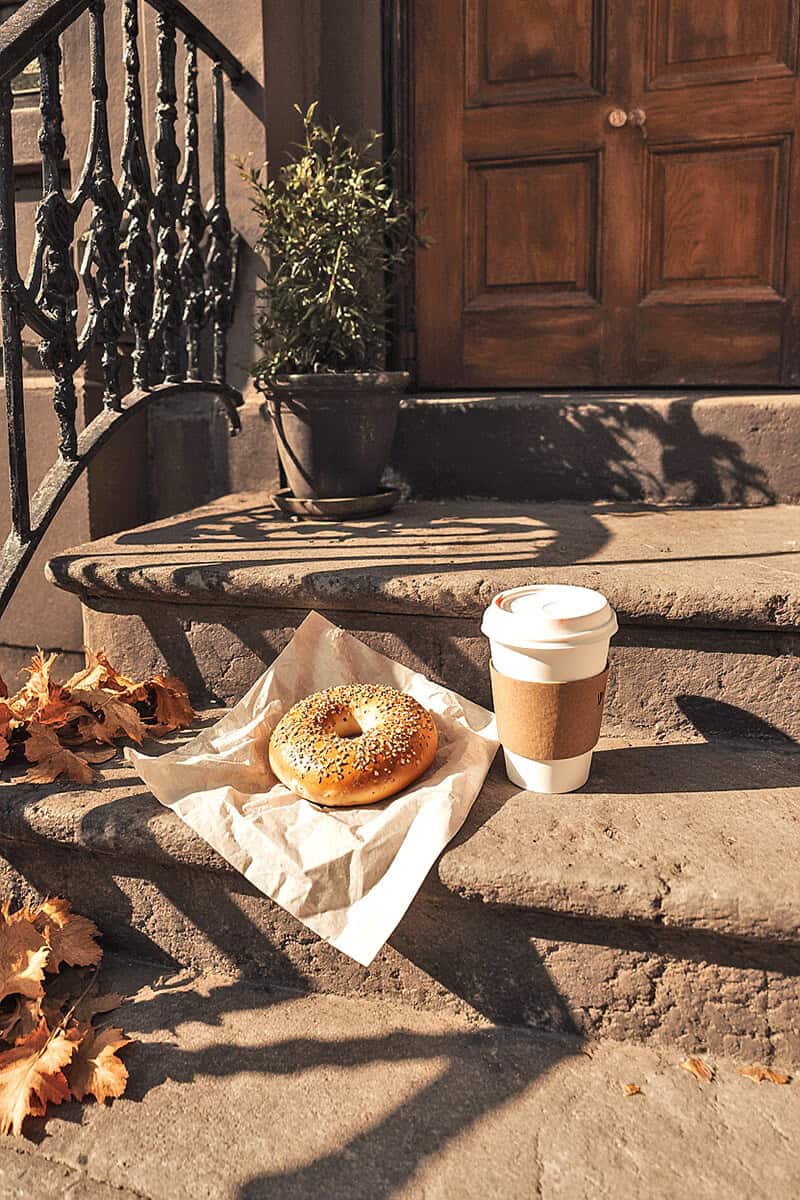 A plain bagel and a coffee on the steps of a Brooklyn house in the fall